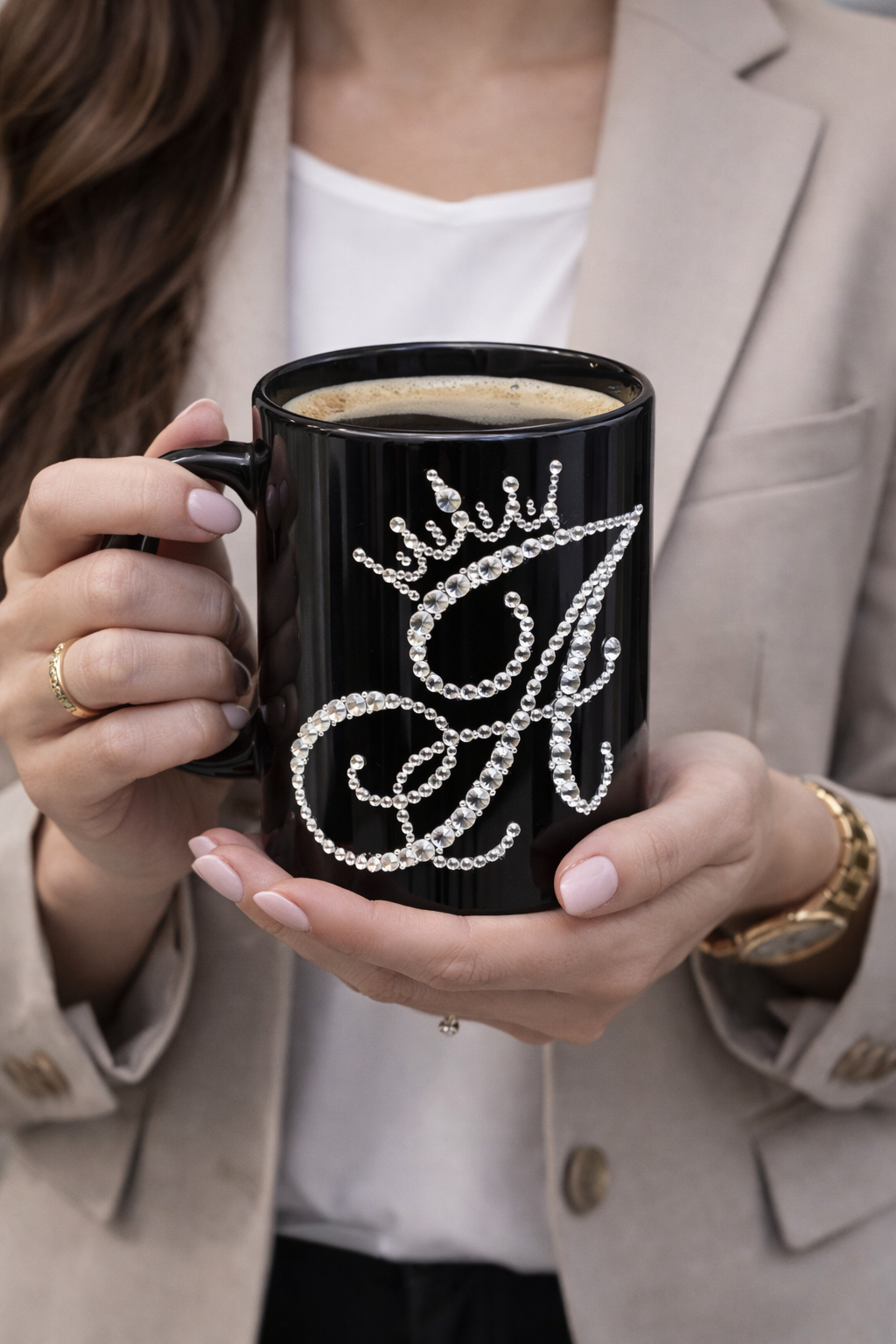 Person holding a black mug with decorative lettering, wearing a beige blazer.